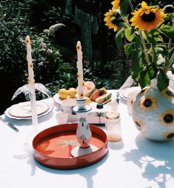 Plateau décoratif carré avec imprimé palmier, aux couleurs vibrantes, posé sur une table avec des bougies et des livres.