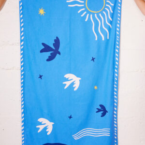 Paréo bleu en coton avec motif "Soleil & Hirondelle", porté à la plage comme robe légère