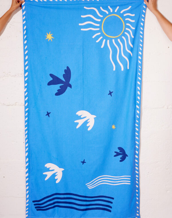 Paréo bleu en coton avec motif "Soleil & Hirondelle", porté à la plage comme robe légère