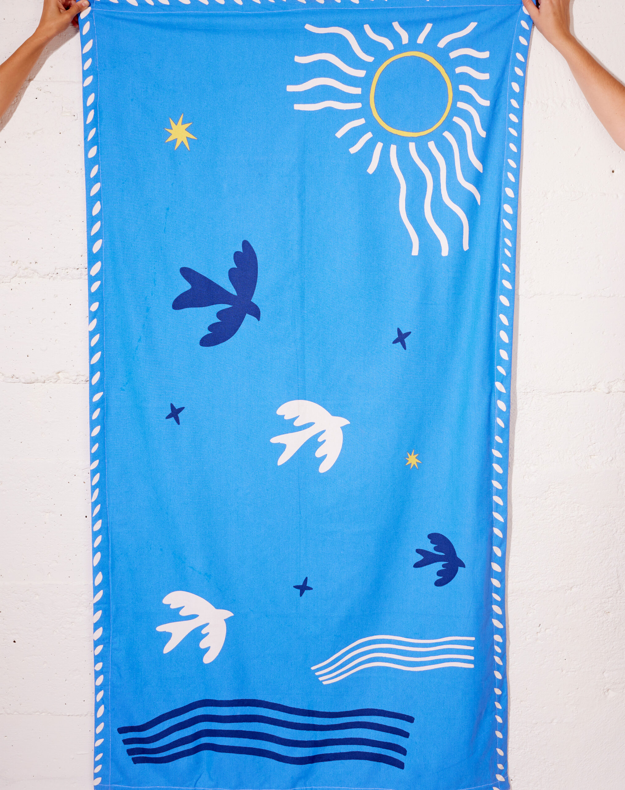 Paréo bleu en coton avec motif "Soleil & Hirondelle", porté à la plage comme robe légère