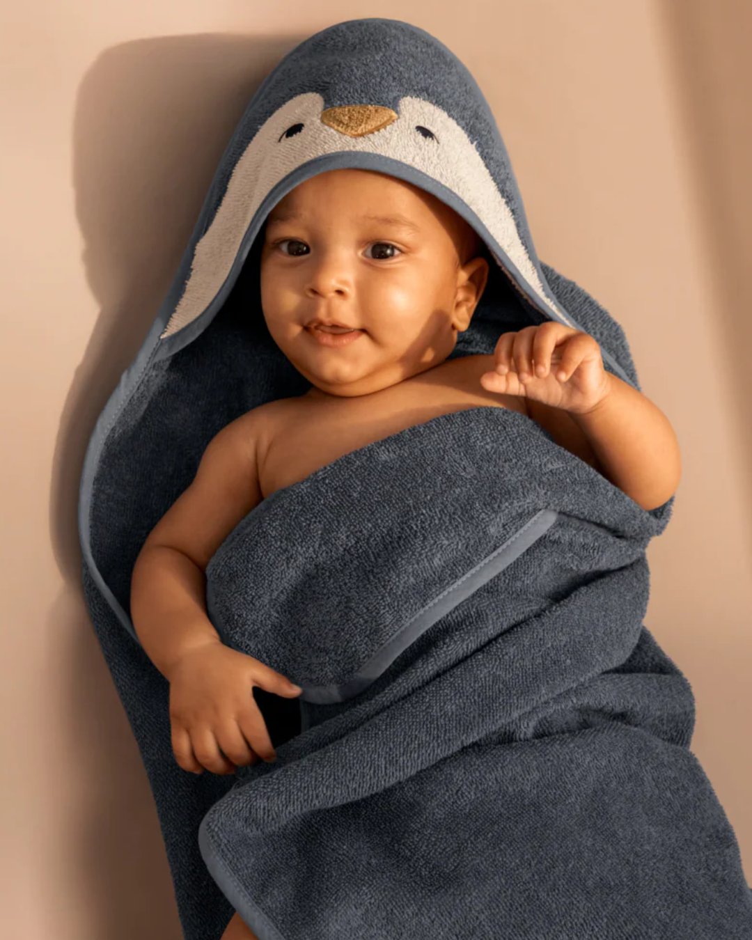 Bébé enveloppé dans une serviette de bain bleue à capuche pingouin en coton biologique GOTS