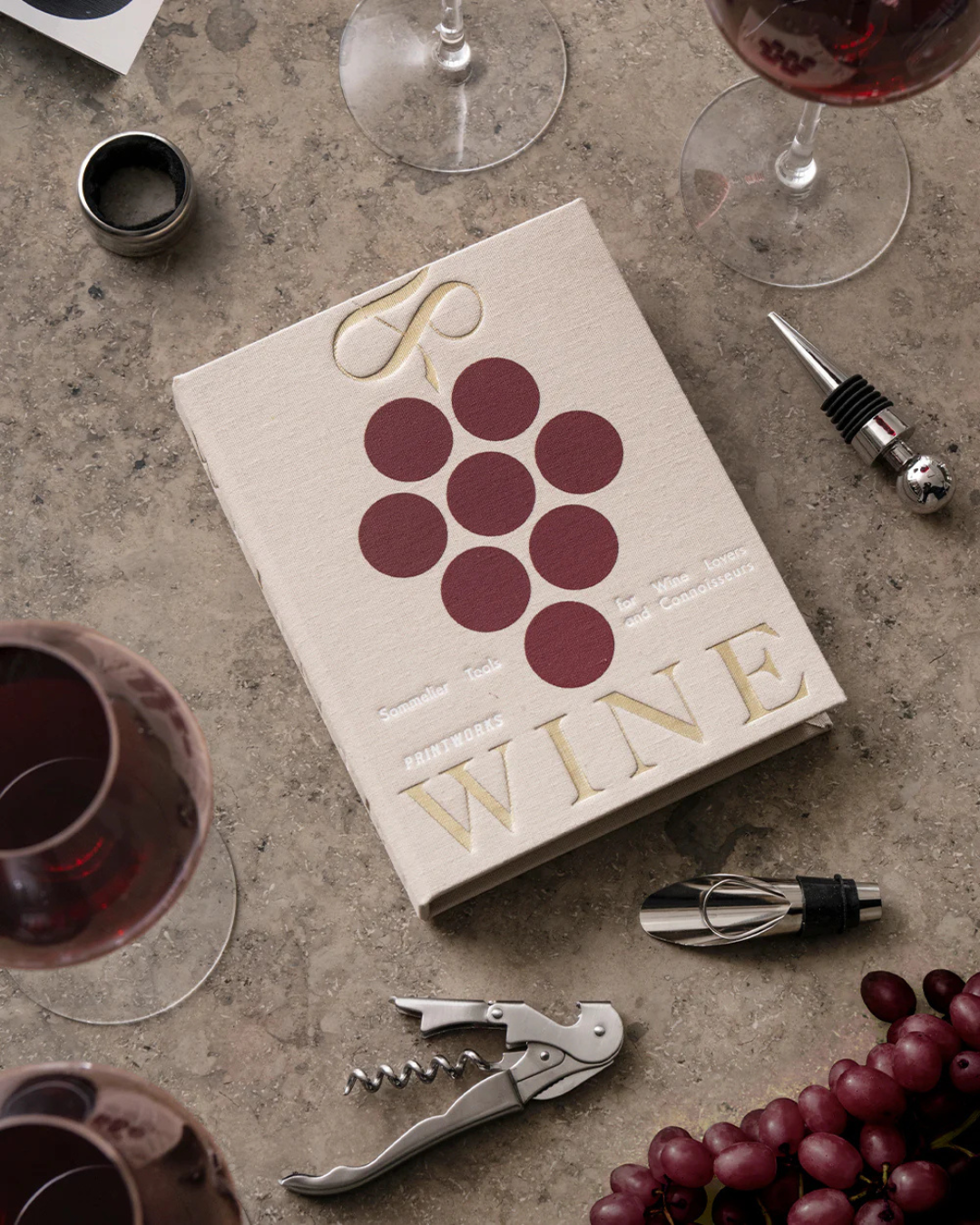 Coffret L’Essentiel du Vin beige en forme de livre, avec tire-bouchon, bouchon, verseur et col anti-gouttes.