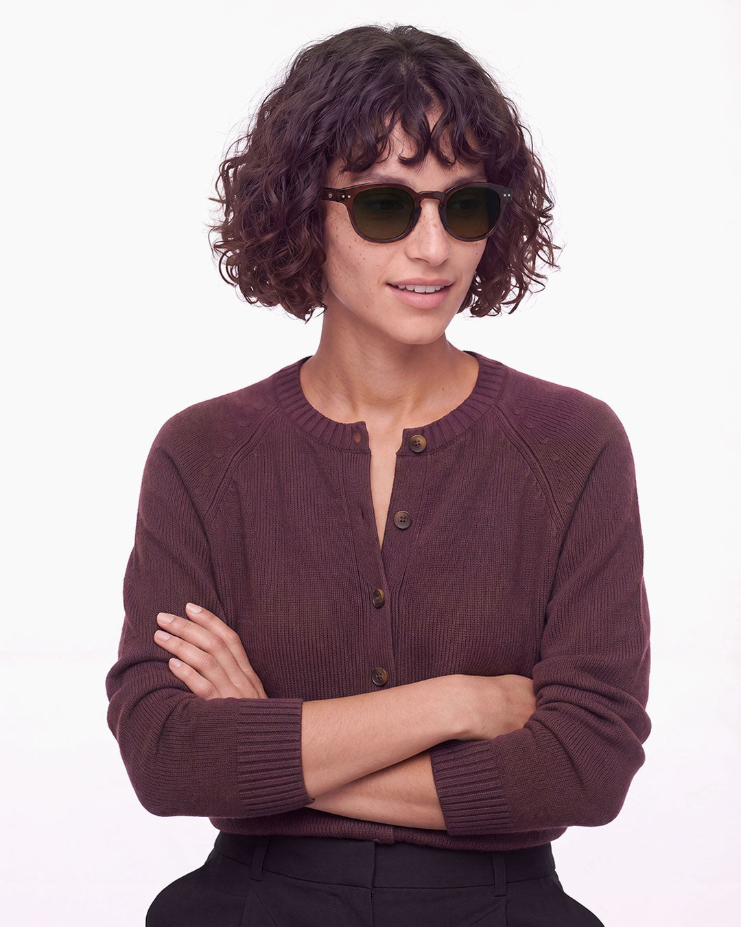 Femme aux cheveux bouclés en gilet bordeaux, bras croisés, portant les lunettes de soleil Izipizi #C Dark Expresso